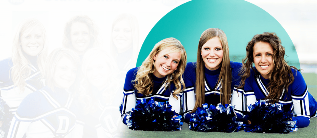 Three smiling cheerleaders in blue and white uniforms posing on the field with blue pom-poms.