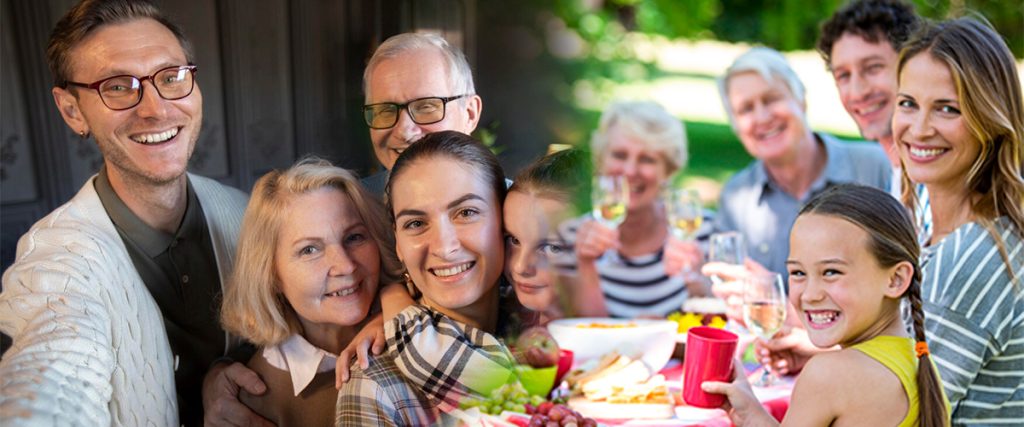 Smiling family gathered together outdoors for a reunion with food and drinks on a picnic table.