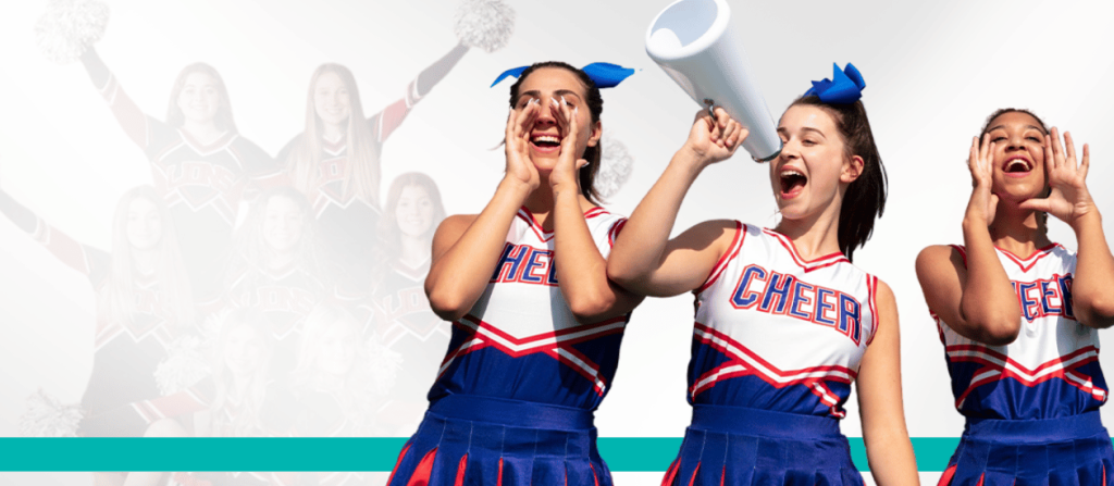 Three enthusiastic cheerleaders in red, white, and blue uniforms, leading cheers with a megaphone under bright sunlight.