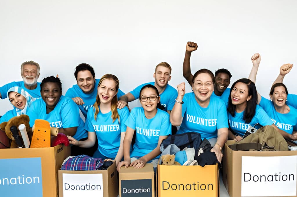 Cheerful group of volunteers in blue shirts posing behind donation boxes filled with items such as clothing and toys.