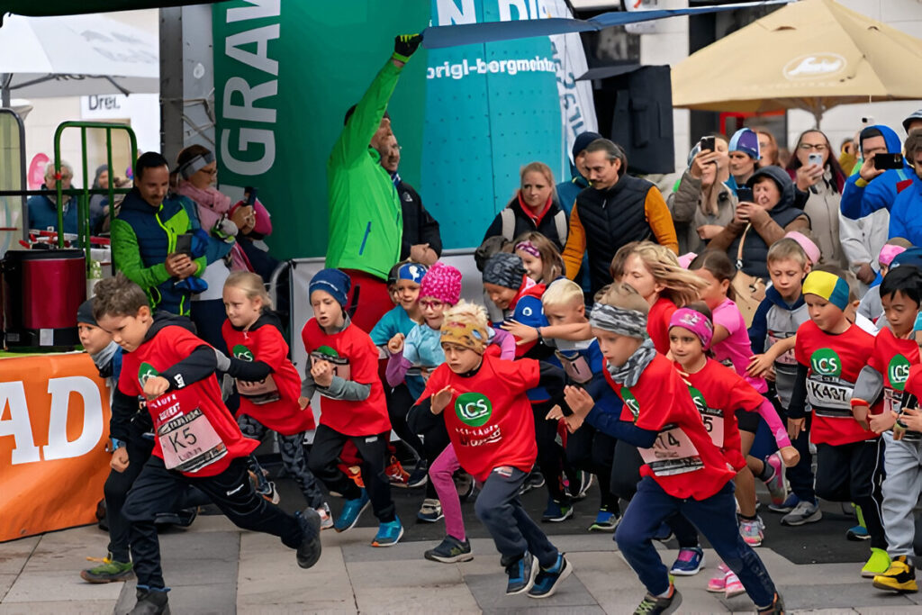 Children in colorful athletic gear starting a fundraising race with a cheering crowd in the background.
