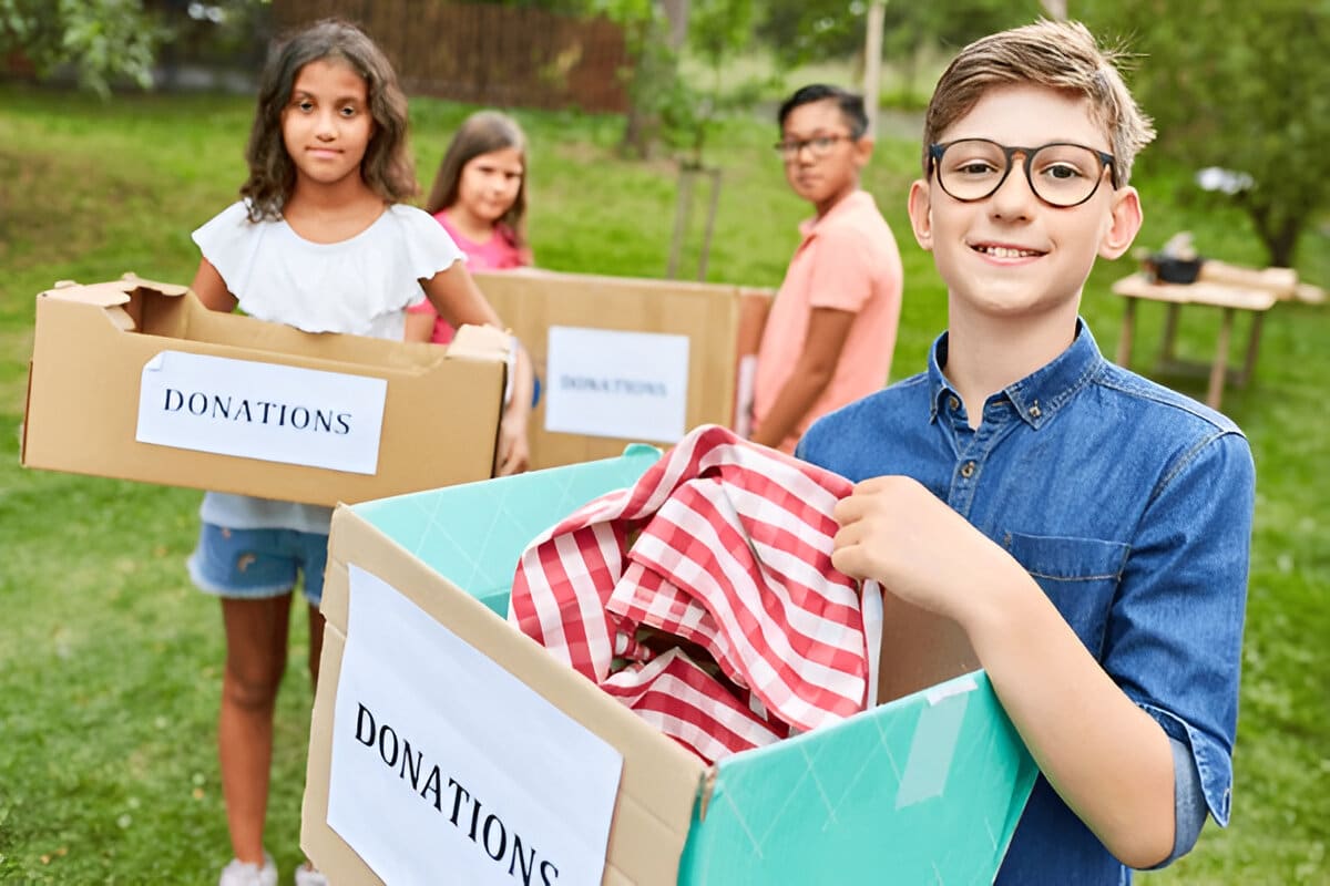 Children holding donation boxes filled with clothes and items in an outdoor setting.