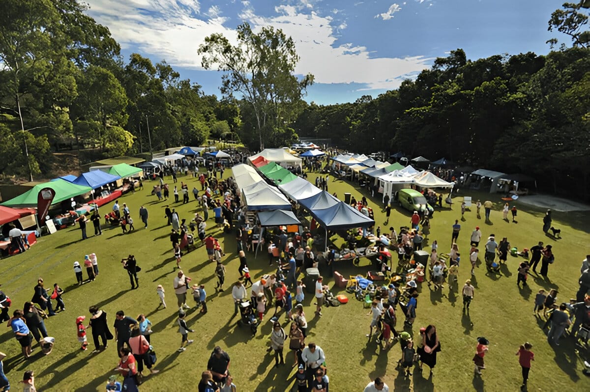 A vibrant outdoor community event with tents, stalls, and attendees gathered on a sunny day.