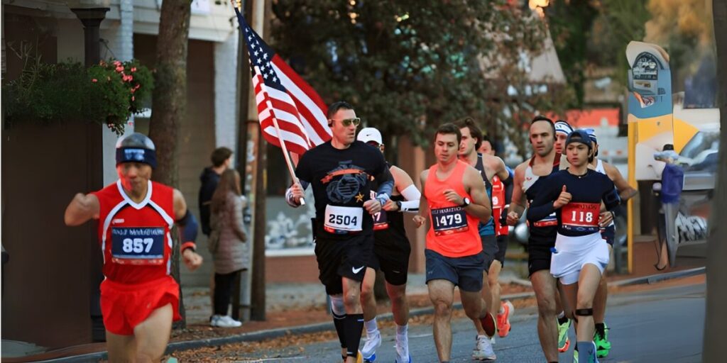 Group of runners in a local marathon, including a participant carrying the American flag, running through a small-town street.
